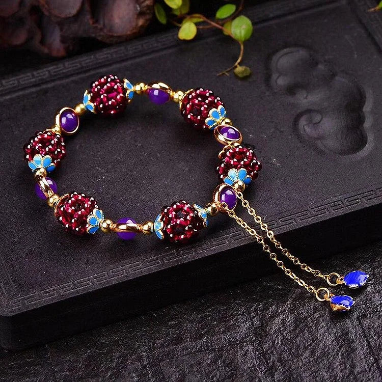 Elegantes Armband mit roten Perlen, blauen Akzenten und goldener Kette auf schwarzem Hintergrund.