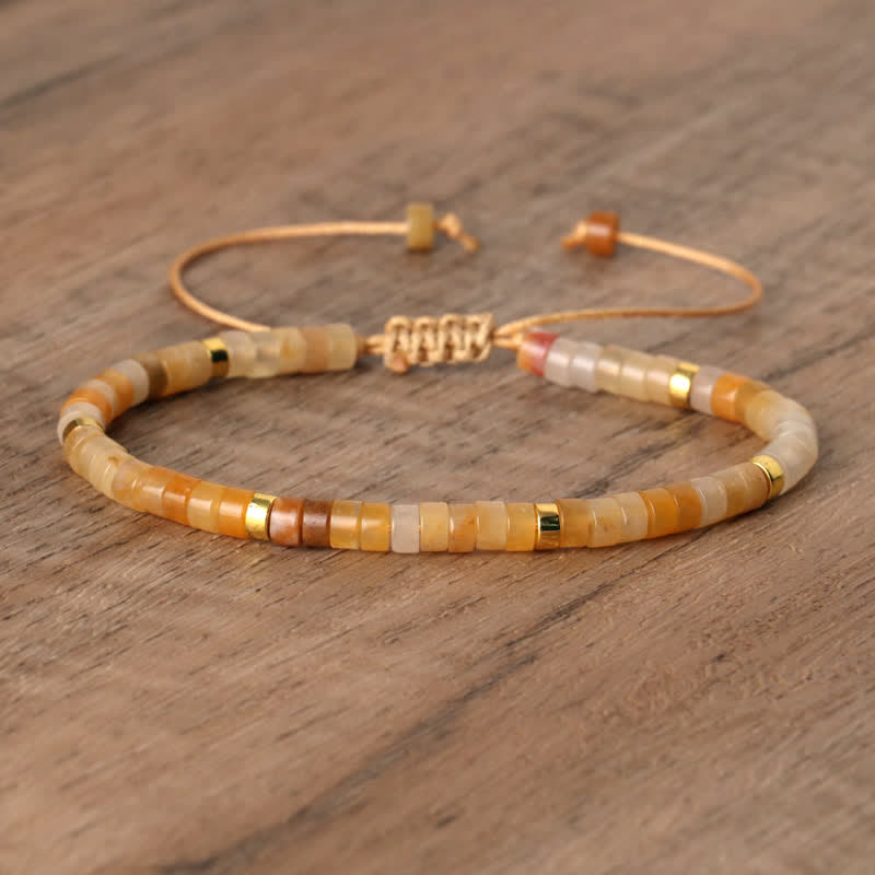 Armband aus Natursteinperlen, beige und gold, verstellbar, handgefertigt, auf Holzoberfläche.