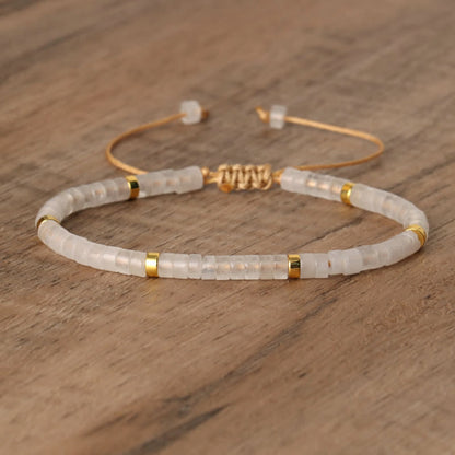 Armband aus weißen Perlen mit goldenen Akzenten auf Holzoberfläche, verstellbar, elegant.