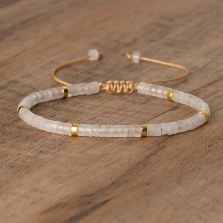 Armband aus weißen Perlen mit goldenen Akzenten auf Holzoberfläche, verstellbar, elegant.