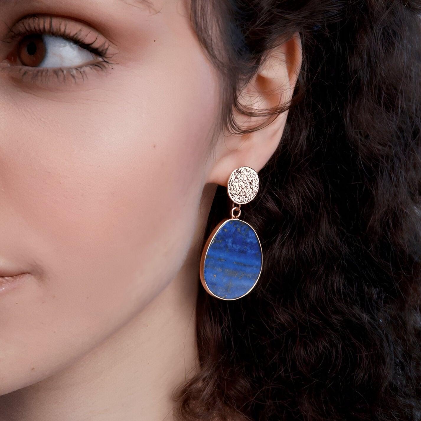 Frau mit blauem Edelstein-Ohrring, oval, goldener Rand, eleganter Schmuck, Nahaufnahme.