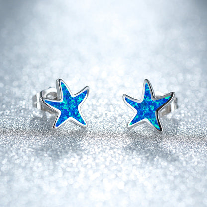Blaue Stern-Ohrringe aus Silber mit Opal-Effekt auf glitzerndem Hintergrund.