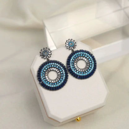 Blaue runde Ohrringe mit Perlen auf weißem Schmuckkästchen, elegantes Design, Damenaccessoire.