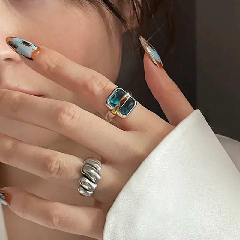 Frau mit blauem Edelsteinring und silbernem Ring, modische Nageldesigns, Nahaufnahme.