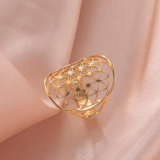 Goldener Ring mit Lebensblume-Muster auf rosa Stoff, eleganter Schmuck, modisches Accessoire.