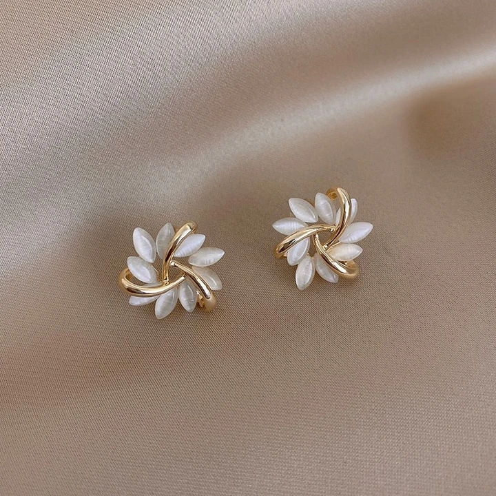 Goldene Ohrringe mit weißen Perlen, Blumenform, auf beigem Stoff, eleganter Schmuck.