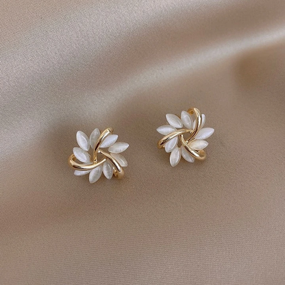 Goldene Ohrringe mit weißen Perlen, Blumenform, auf beigem Stoff, eleganter Schmuck.