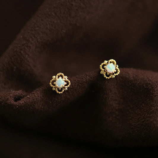 Goldene Ohrringe mit Opal, Blumenform, auf braunem Stoff, eleganter Schmuck, Damenaccessoire.