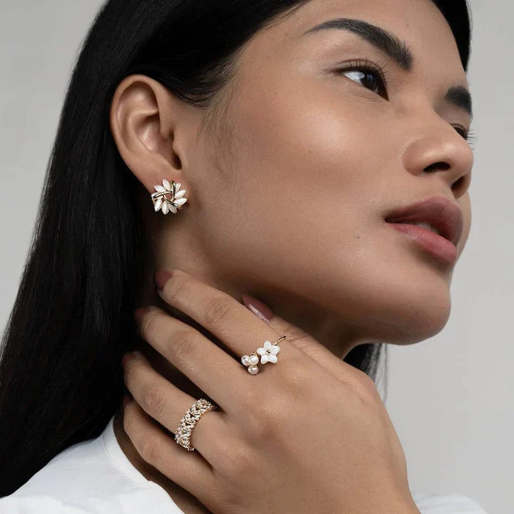 Frau mit goldenen Ohrringen und Ringen, Blumenmotiv, eleganter Schmuck, Nahaufnahme.