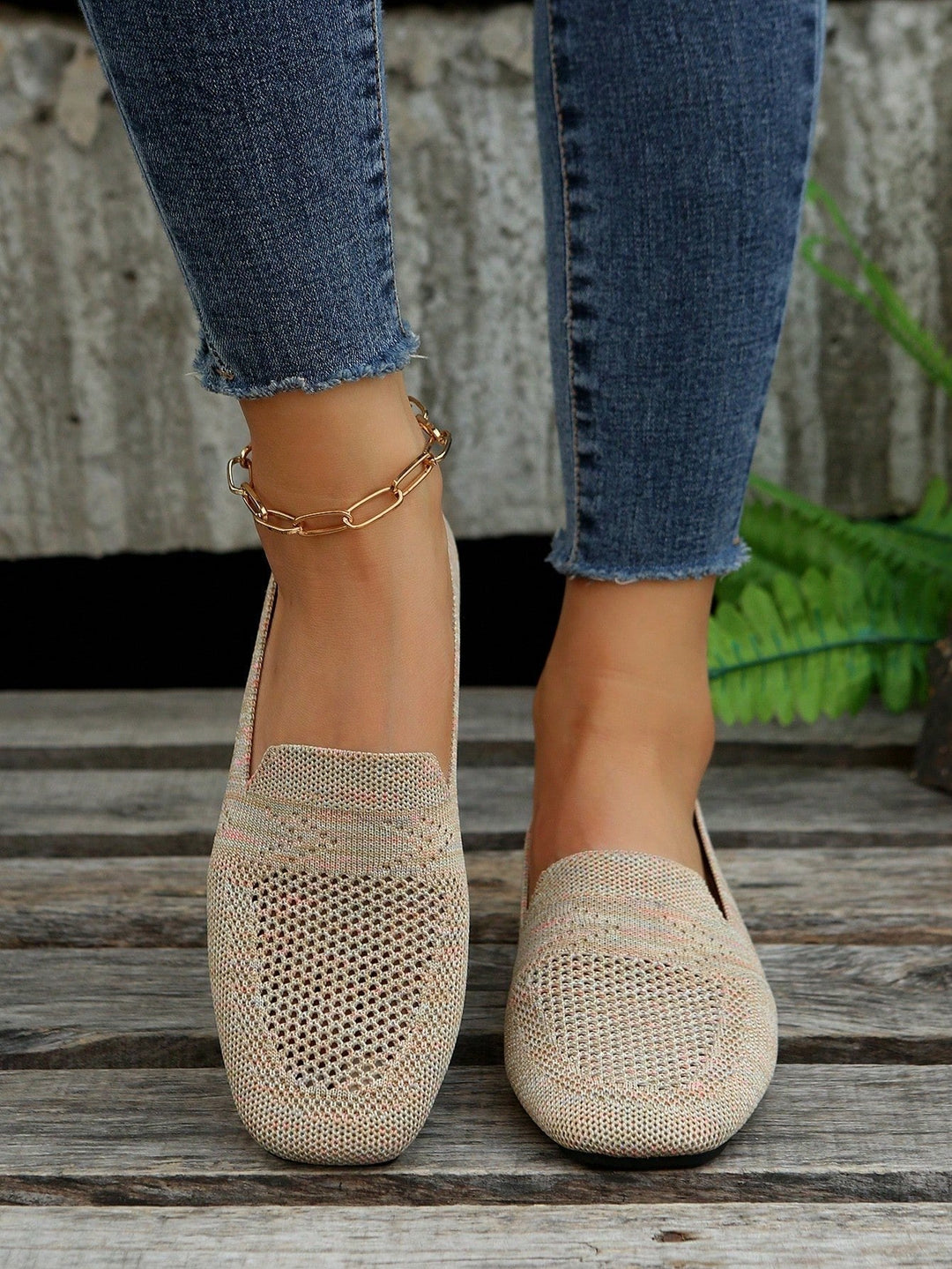 Beige strikkede slip-on sko med hulmønster og lyserøde striber, set forfra på model i jeans på trægulv. 3