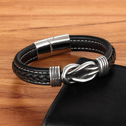 Schwarzes Lederarmband mit silbernem Knotenverschluss auf Holztisch. Herrenschmuck Accessoire.