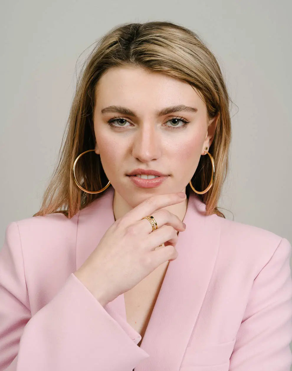Frau mit großen goldenen Creolen, rosa Blazer, modischer Schmuck, eleganter Look.