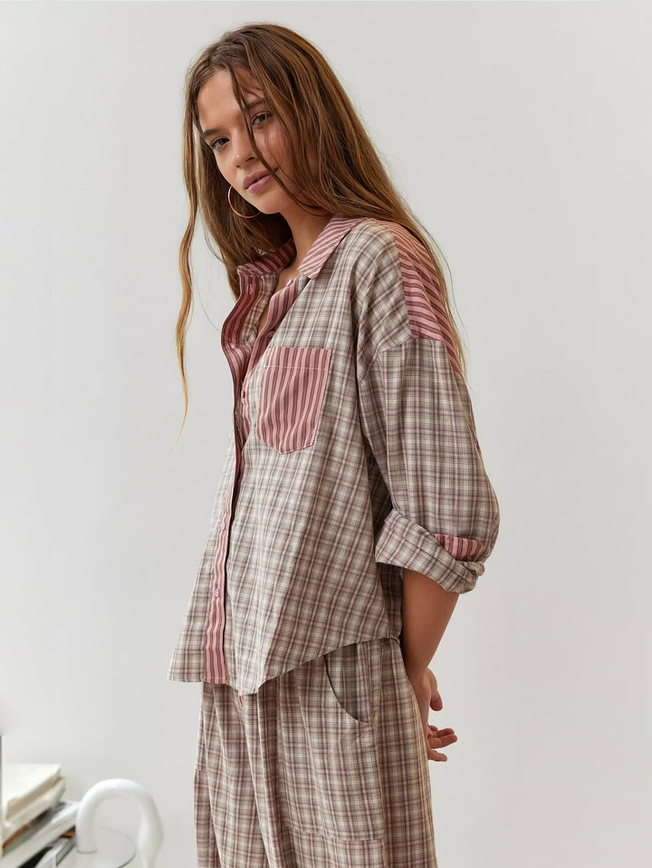 Model i lyserød og beige ternet pyjamasskjorte med stribet lomme og krave, set fra siden med hænderne bag ryggen. 2