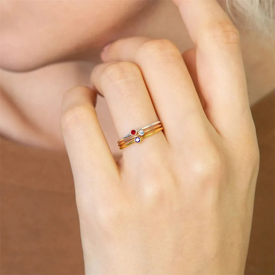 Damenhand mit drei goldenen Ringen, verziert mit roten und blauen Edelsteinen.