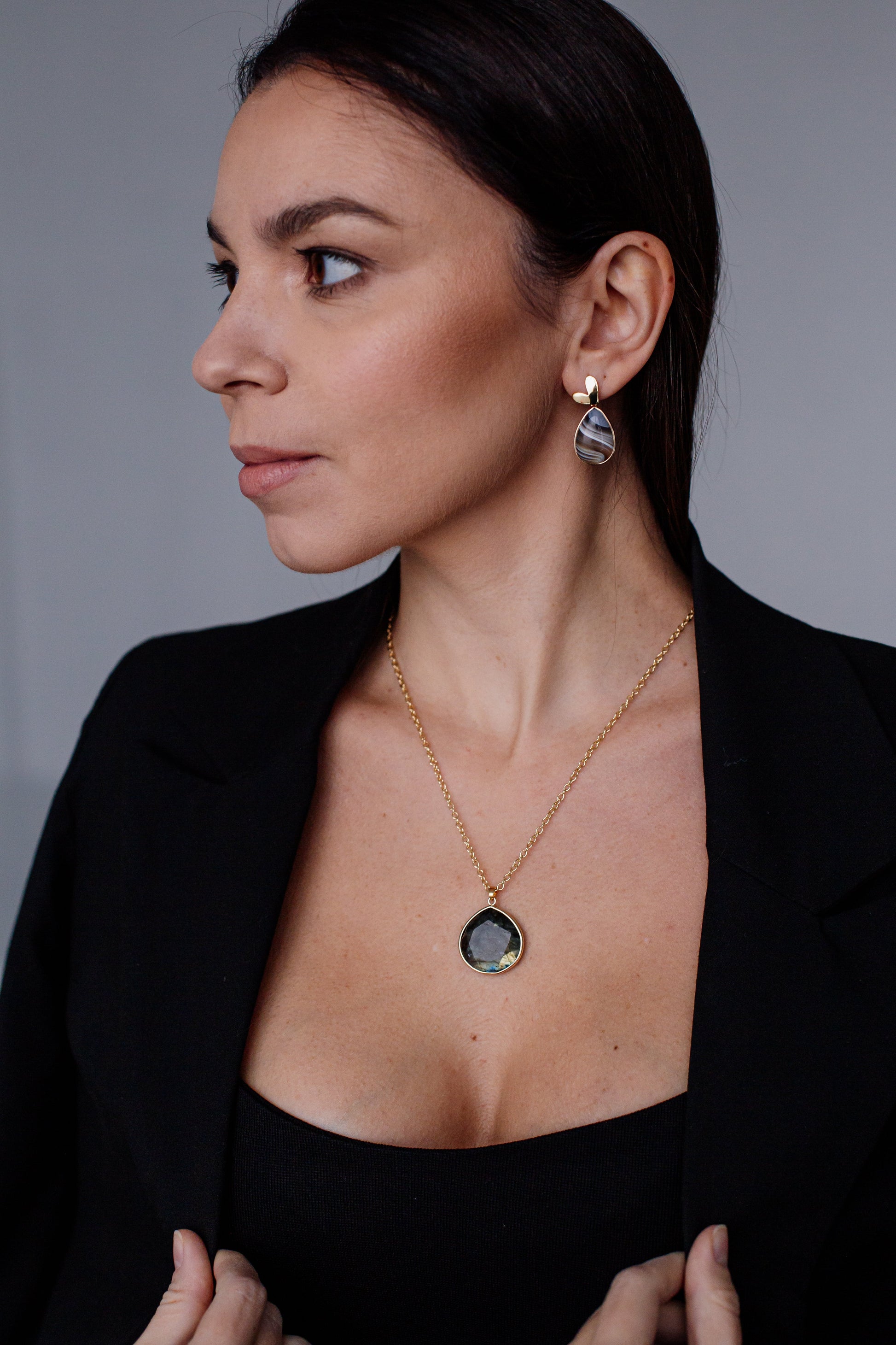 Frau mit schwarzem Blazer, goldener Halskette und Ohrringen, eleganter Schmuck, Porträtaufnahme.