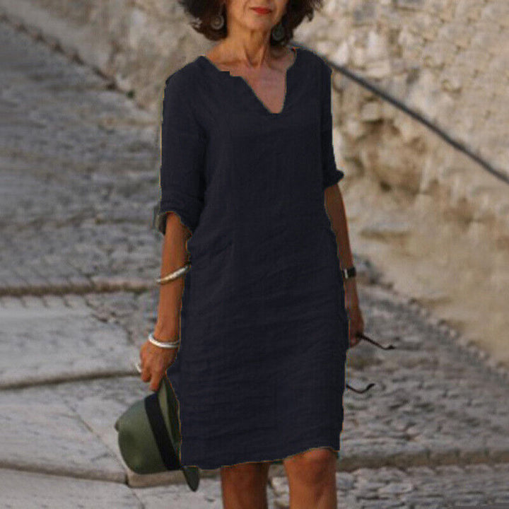 Frau in schwarzem Leinenkleid, V-Ausschnitt, auf Kopfsteinpflasterweg, Sommermode.