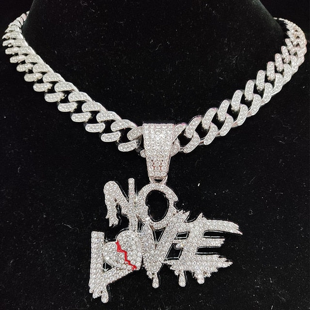 Silberne Halskette mit "No Love"-Anhänger, besetzt mit funkelnden Kristallen, auf schwarzem Hintergrund.