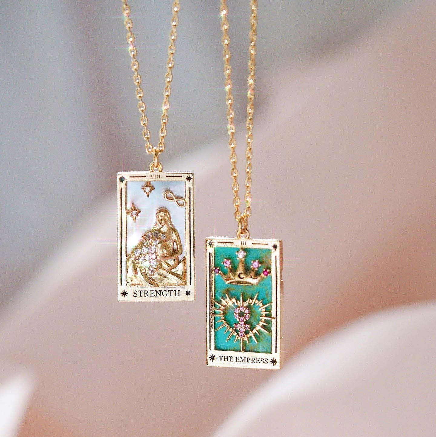 Zwei goldene Tarot-Halsketten mit "Strength" und "The Empress" Anhängern, verziert mit Edelsteinen.
