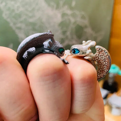 Zwei Eidechsen-Ringe, silber und bronze, mit blauen Augen, auf einer Hand getragen.