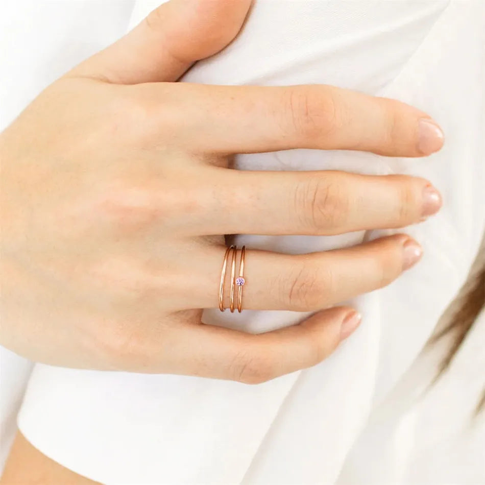 Damenhand mit drei goldenen Ringen, einer mit kleinem rosa Edelstein, auf weißem Hintergrund.