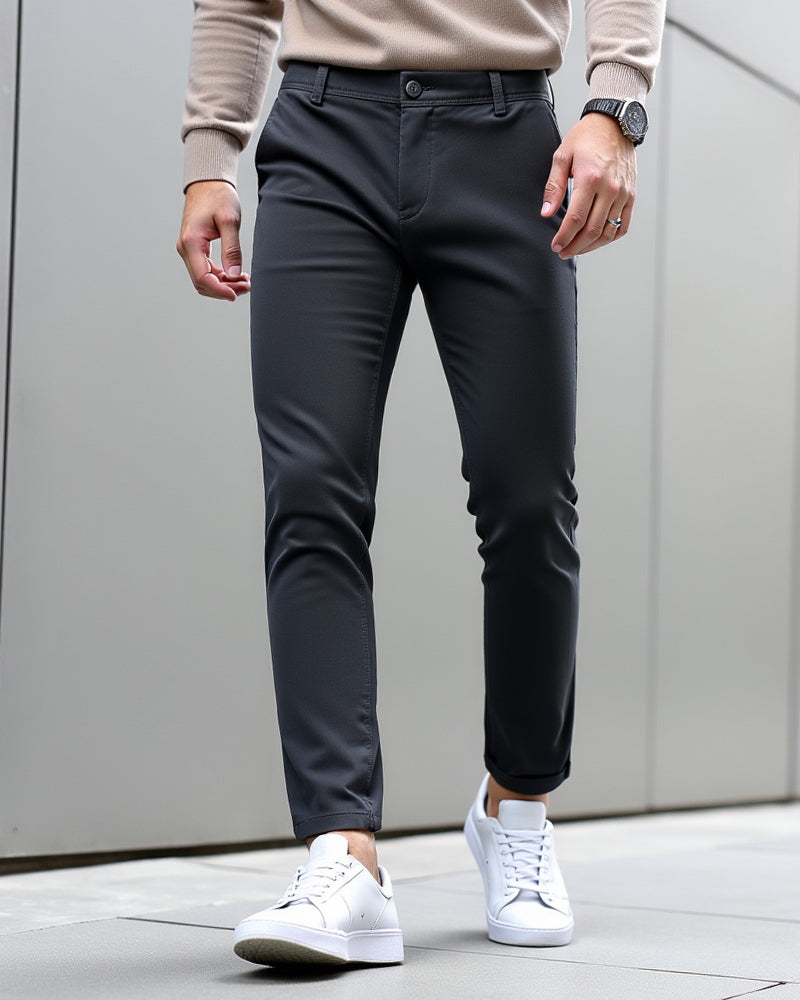 Mørkegrå chinos med oprullet benkant, båret med beige strik, armbåndsur og hvide sneakers foran en grå væg. 9