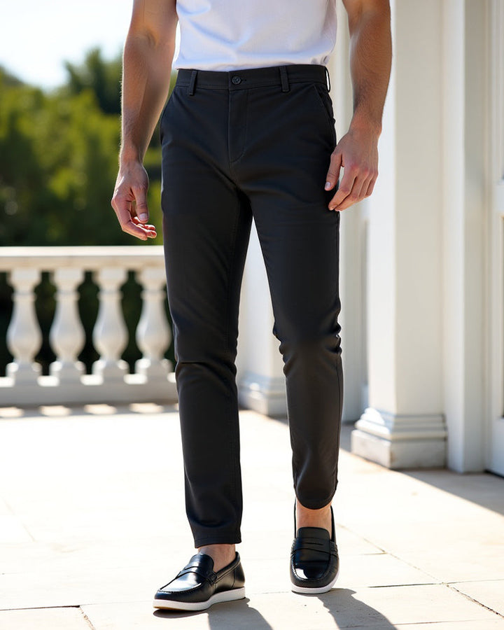 Mørkegrå chinos båret med hvid t-shirt og sorte loafers på en solbeskinnet terrasse med hvide søjler. 7