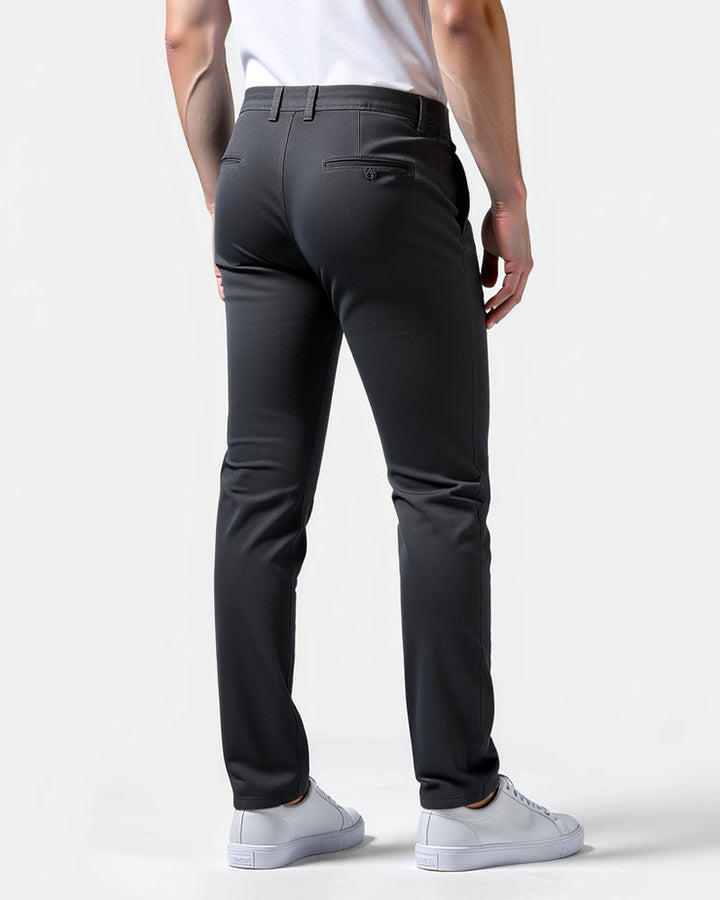 Mørkegrå chinos set bagfra på model med hvide sneakers, to baglommer med knap og bælteløkker. 8