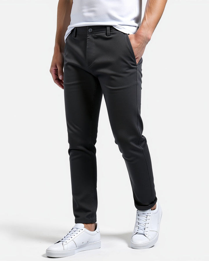 Mørkegrå slim fit chinos set fra siden på model med hvid t-shirt, hvide sneakers og hånden i lommen. 6
