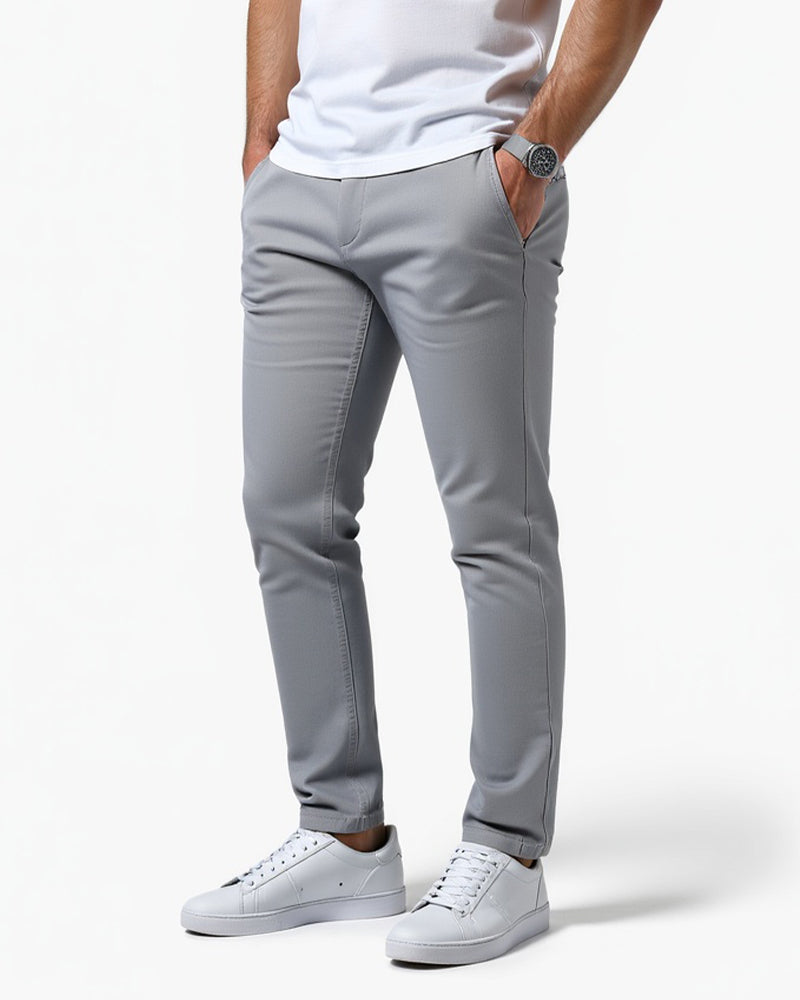 Lysegrå slim fit chinos set fra siden på model med hvid t-shirt, hvide sneakers og hånden i lommen. 1