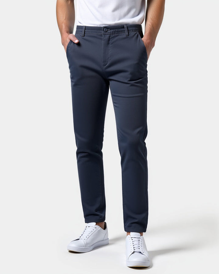 Marineblå slim fit chinos set forfra på model med hvid t-shirt, hvide sneakers og hænderne i lommerne. 15