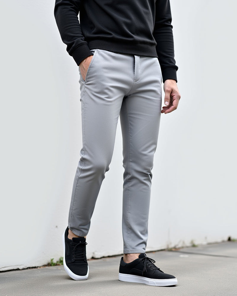 Lysegrå chinos båret med sort sweatshirt og sorte sneakers foran en hvid væg, set forfra og let fra siden. 2