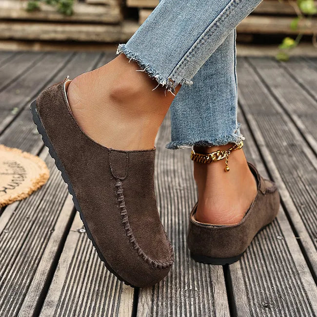 Brune slip-ons set fra siden og bagfra under gang, med åben hæl, flad sort sål og frynsede cowboybukser. 6