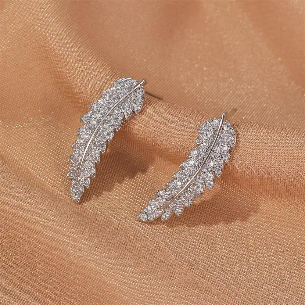 Silberne Blatt-Ohrringe mit Strasssteinen auf beigem Stoff, eleganter Schmuck für Damen.