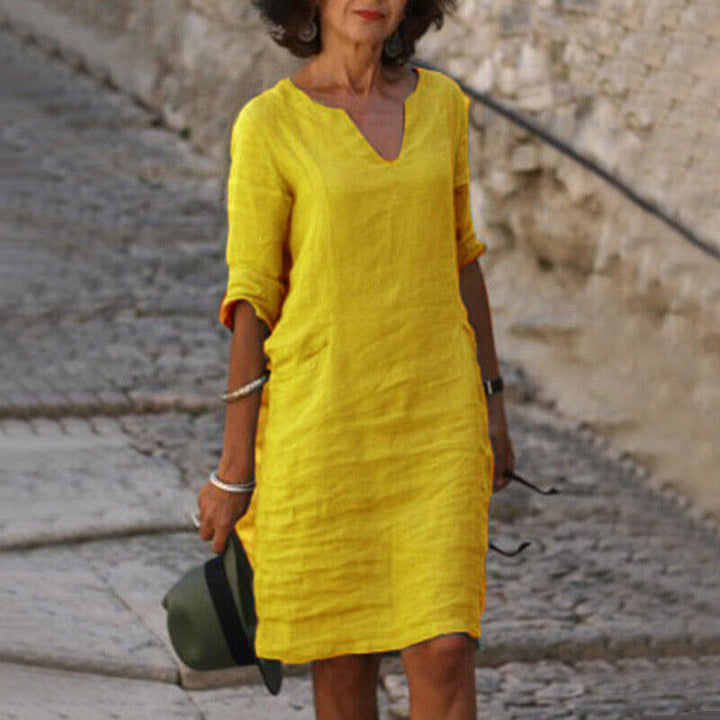 Frau in gelbem Leinenkleid, V-Ausschnitt, knielang, Sommermode, lässig, elegant.