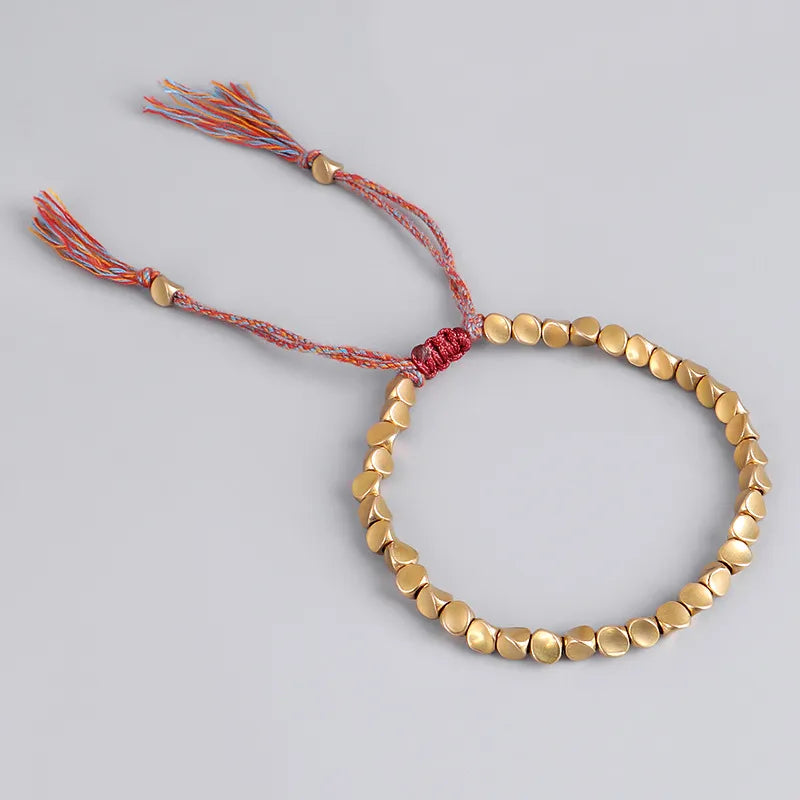 Goldfarbenes Armband mit runden Perlen und buntem Kordelverschluss, handgefertigter Schmuck.