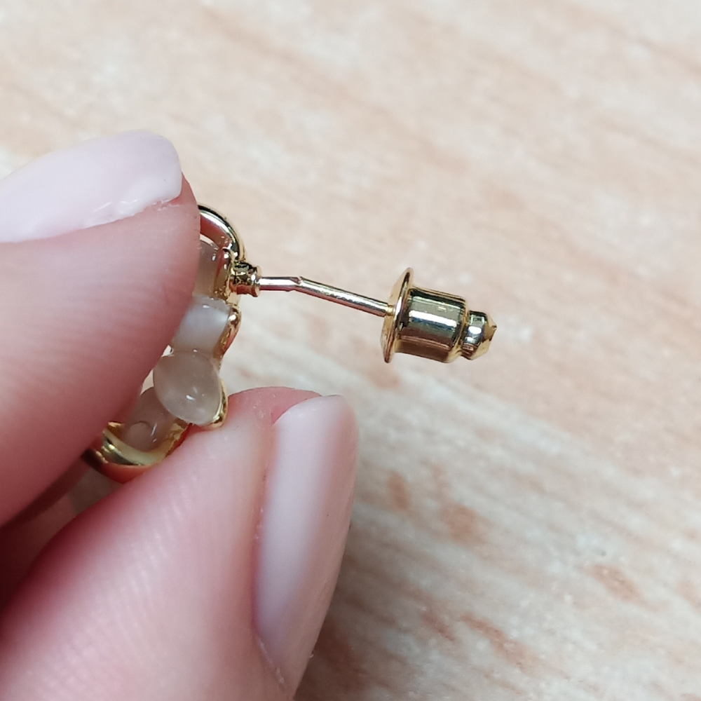 Goldener Ohrring mit Perlen, Nahaufnahme, Hand hält Schmuckstück, elegantes Accessoire.