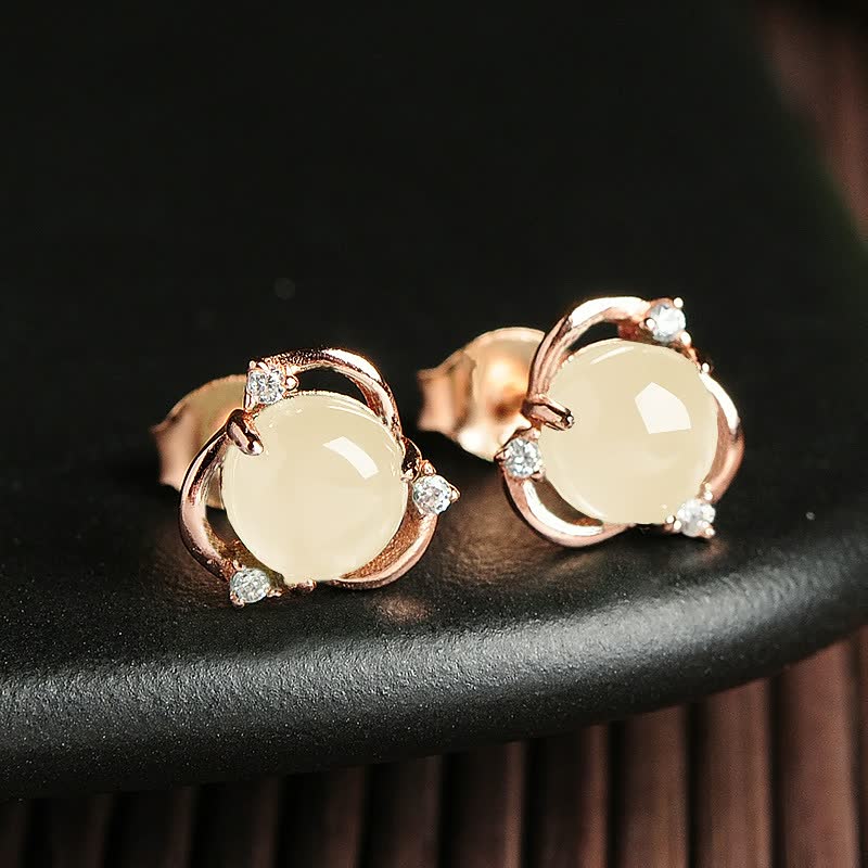 Goldene Ohrringe mit runden, cremefarbenen Steinen und kleinen Diamanten auf schwarzem Hintergrund.