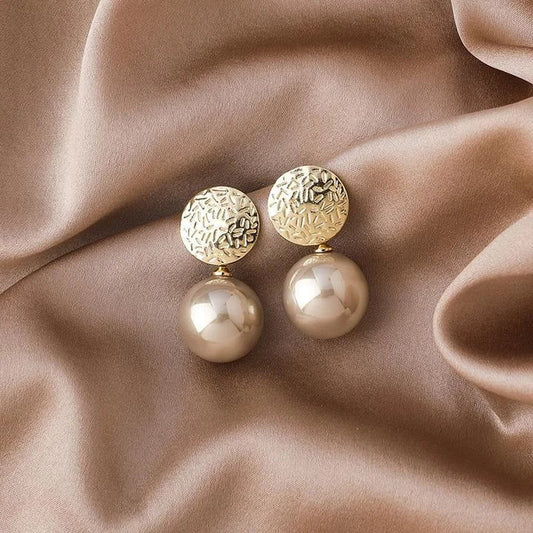 Goldene Ohrringe mit Perlen auf beigem Seidenstoff, eleganter Schmuck, modisches Accessoire.