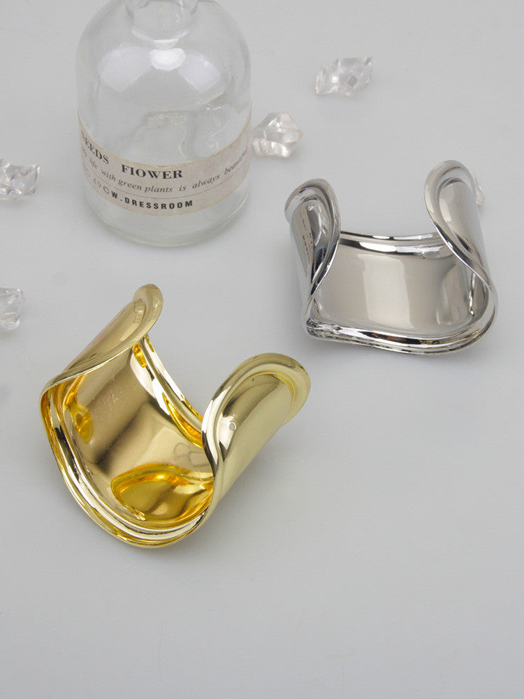 Goldenes und silbernes Metallarmband, asymmetrisches Design, modisch, auf weißem Hintergrund.