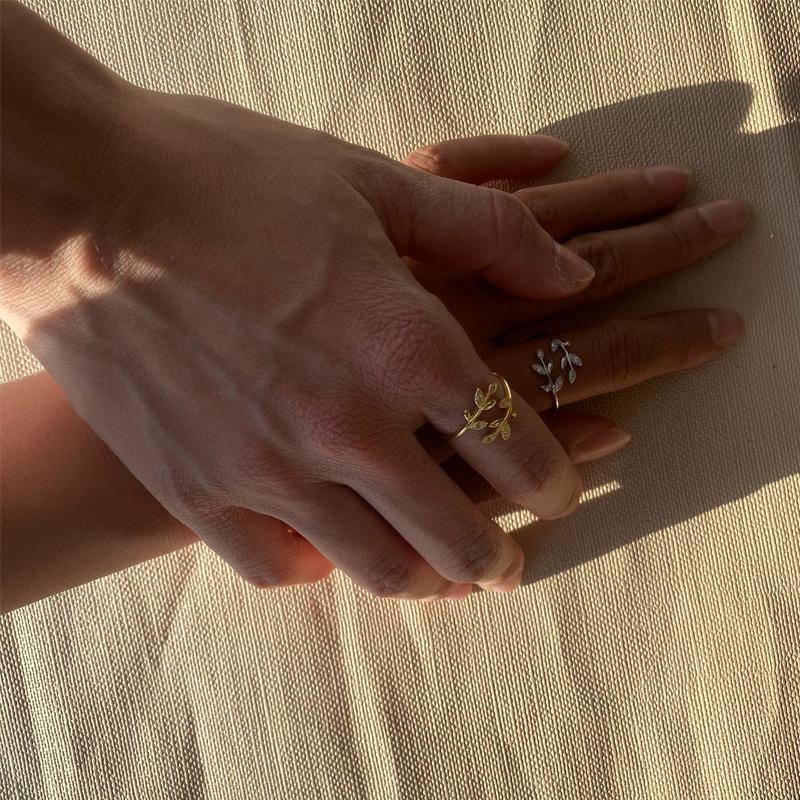 Zwei Hände mit goldenen und silbernen Blatt-Ringen auf beigem Stoff.