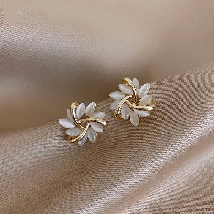 Goldene Ohrringe mit weißen Blättern auf beigem Satin-Hintergrund, eleganter Schmuck.
