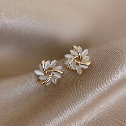 Goldene Ohrringe mit weißen Blättern, elegantes Design, Schmuck auf beigem Stoff.