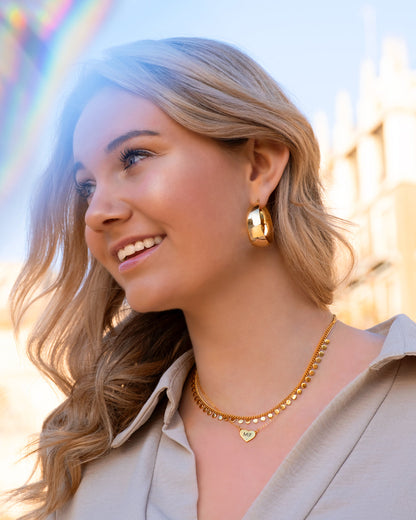 Frau mit goldenen Statement-Creolen und Halskette, lächelnd im Freien.