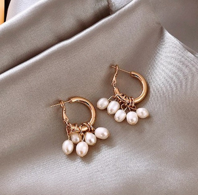 Goldene Ohrringe mit Perlenanhängern auf grauem Stoff, eleganter Schmuck für Damen.