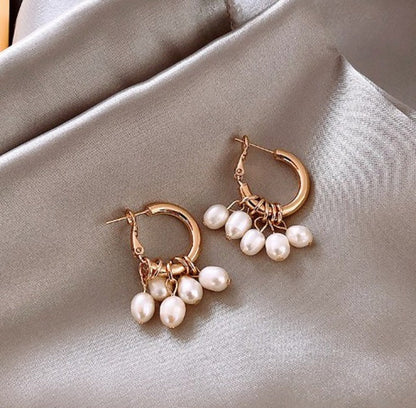 Goldene Ohrringe mit Perlenanhängern auf grauem Stoff, eleganter Schmuck für Damen.