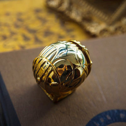Goldener, kunstvoll verzierter Metallring auf Holzoberfläche, elegantes Schmuckdesign.