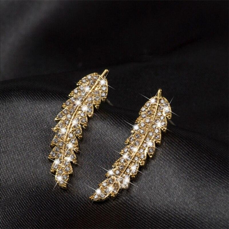 Goldene Feder-Ohrringe mit Strasssteinen auf schwarzem Hintergrund, eleganter Schmuck.