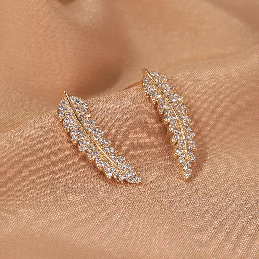 Goldene Ohrringe mit Strasssteinen, blattförmig, auf beigem Stoff, eleganter Schmuck.