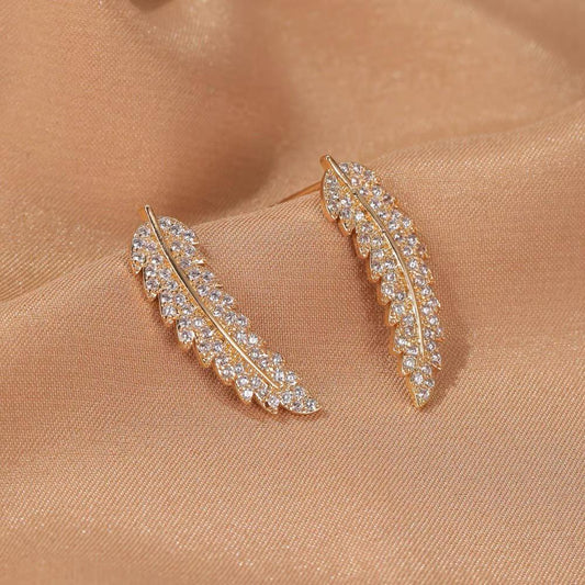 Goldene Ohrringe mit Strasssteinen, blattförmig, auf beigem Stoff, eleganter Schmuck.