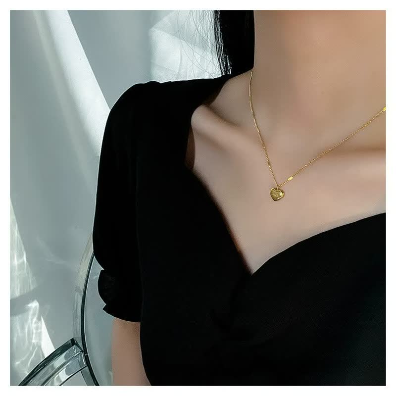 Frau mit schwarzem Kleid trägt goldene Herz-Halskette, eleganter Schmuck, minimalistisch.